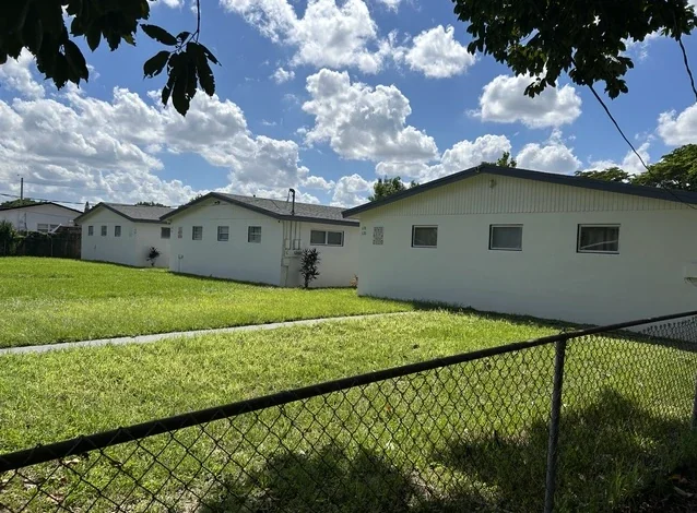 Three single-story white multifamily buildings on a large lawn on SW 4th Avenue, Hallandale Beach